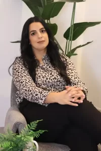 אירית שלום, מאמנת נשים לאחר אובדן, יושבת בכורסה לובשת חולצת מנומרת וידיים שלובות