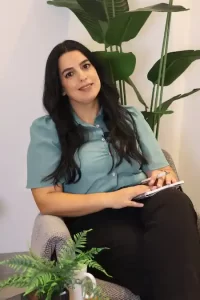 אירית שלום, מאמנת נשים לאחר אובדן, יושבת בכורסה לובשת חולצה טורקיז ומחזיקה פנקס ועט